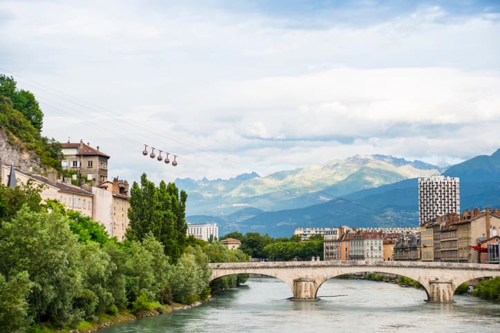 City of Grenoble city buildings on the banks of the river Isere showing bridge over the water and blue sky