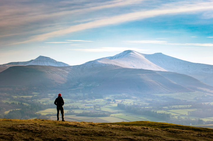 Person standing on top of the Brecon Beacons in Wales with mountains in background