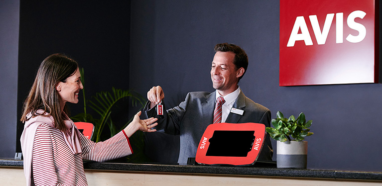 An Avis customer is handed his key by a rental sales agent at the counter