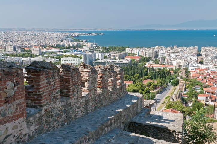 Thessaloniki street scene with castle walls and road with buildings leading to sea with blue sky behind
